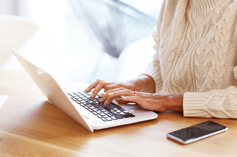 Woman wearing a cream colored sweater typing on a laptop.